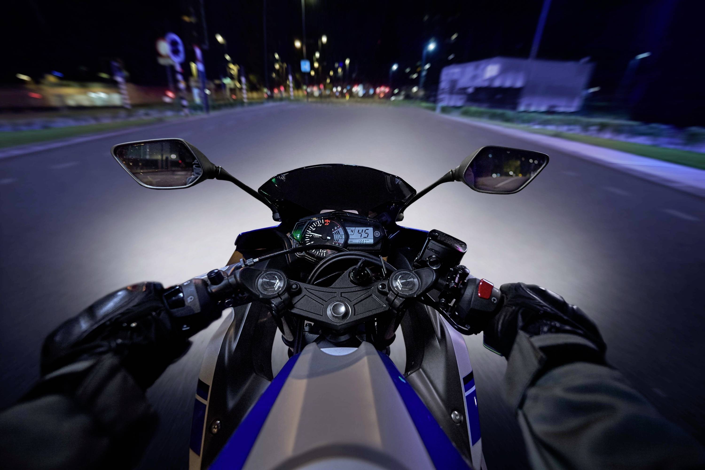Vue depuis la perspective d'un motocycliste la nuit, concentrée sur le guidon, l'indicateur de vitesse affiche 45 km/h.