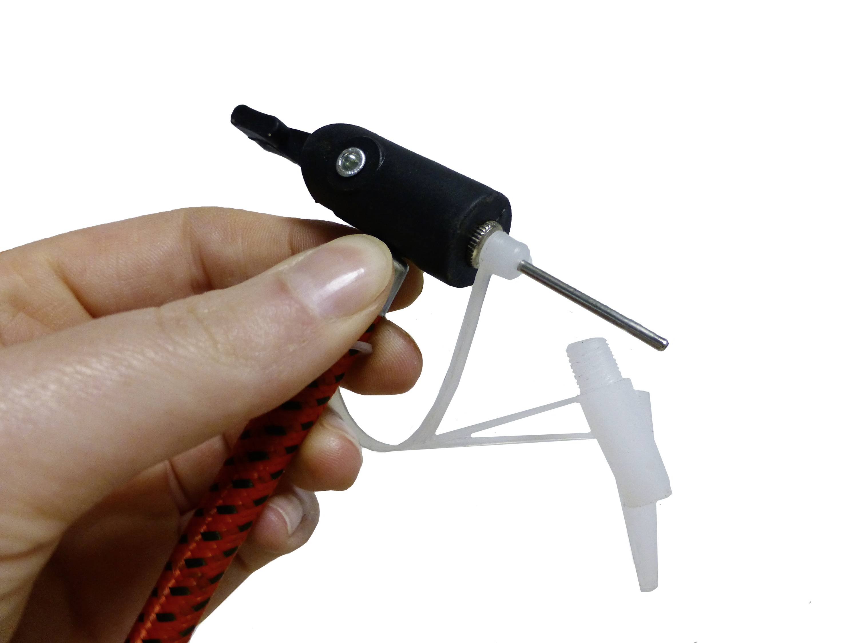 Main tenant un petit moteur électrique noir avec une poignée rotative, raccordé à un tuyau en plastique blanc et à une buse. Usage inconnu.