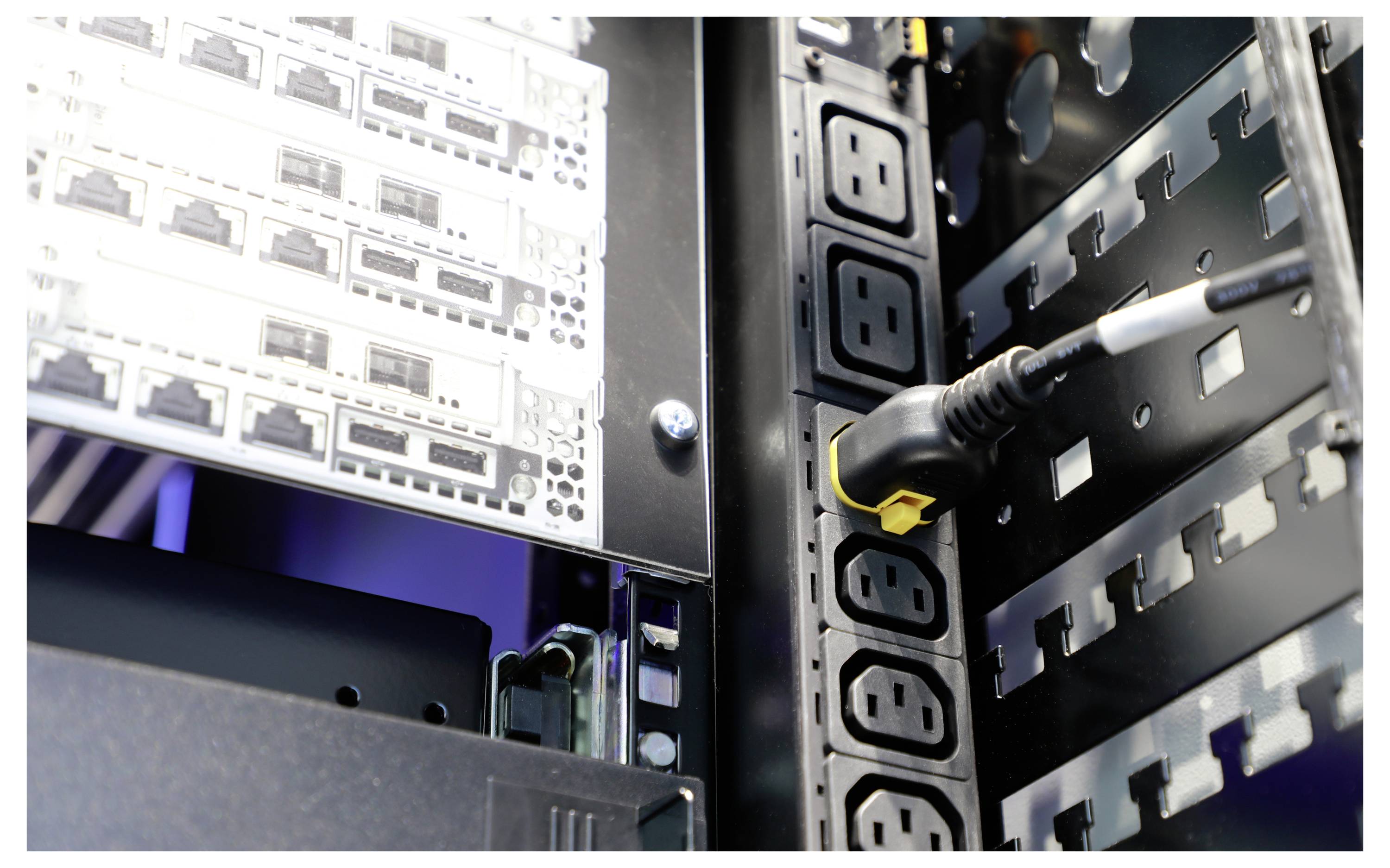 Une armoire de salle de serveurs montre des serveurs et des dispositifs de connexion électrique installés dans un rack. Un câble est branché à une prise de courant.
