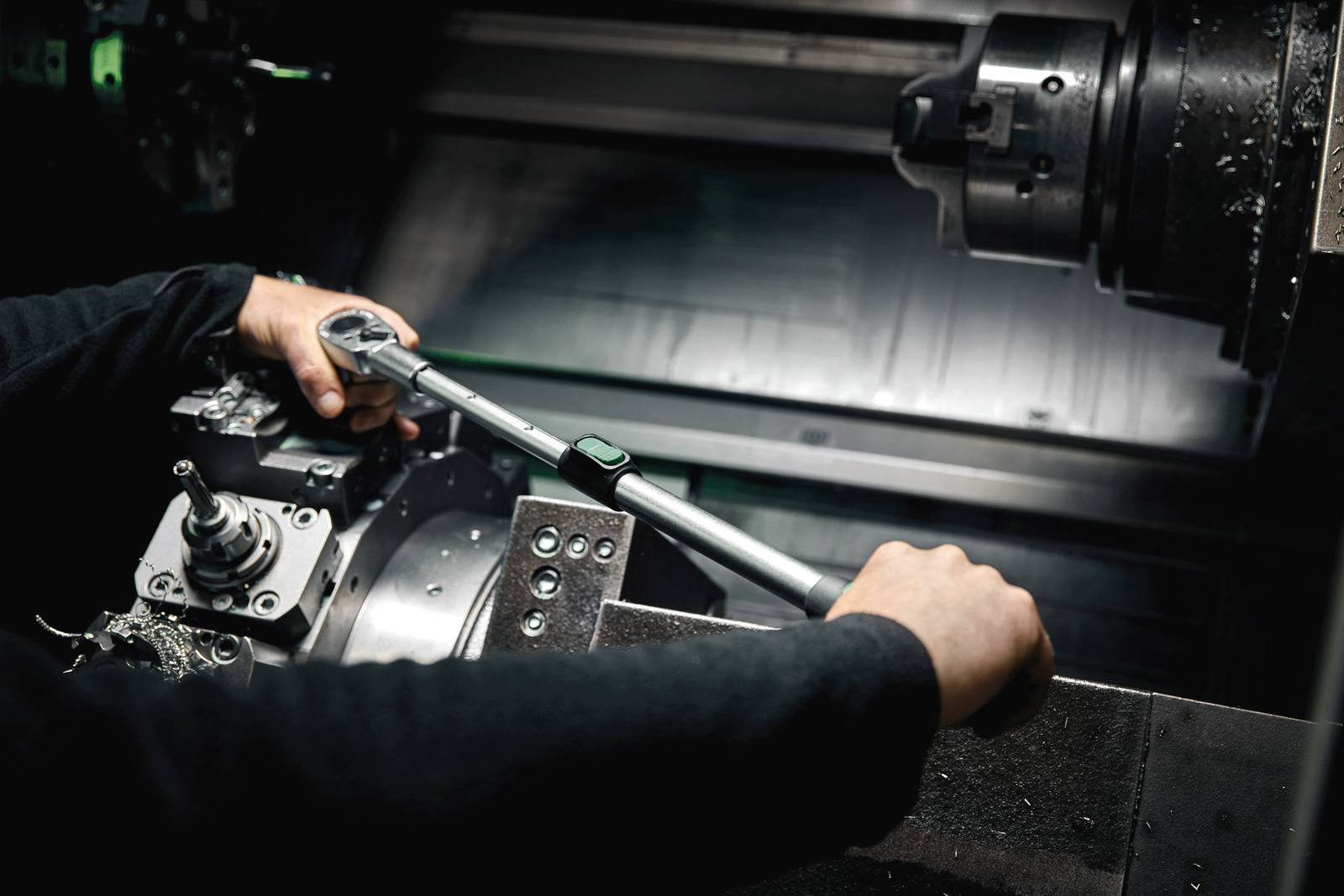 Une personne utilise une clé dynamométrique pour l'entretien ou la réparation d'une machine, avec les mains et certaines parties de la machine visibles.