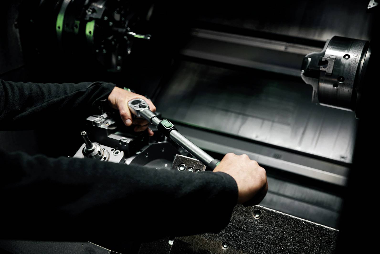 Une personne travaille sur une machine CNC dans une pièce sombre. Elle tient un outil et ajuste délicatement un composant métallique.