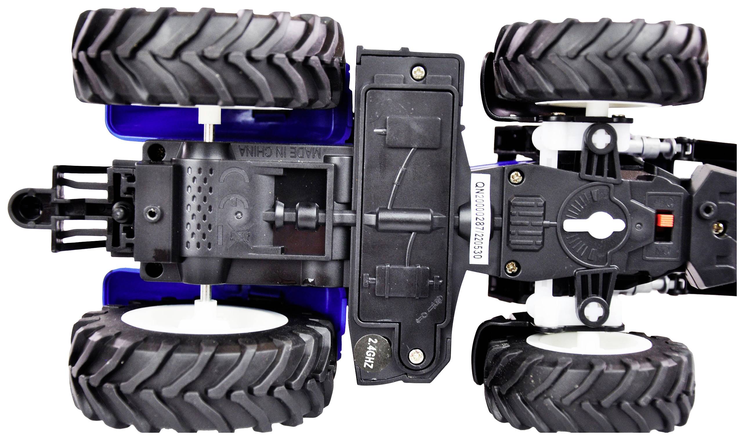 Un tracteur-jouet est couché à l'envers sur un fond blanc, ses grandes roues noires bien visibles.