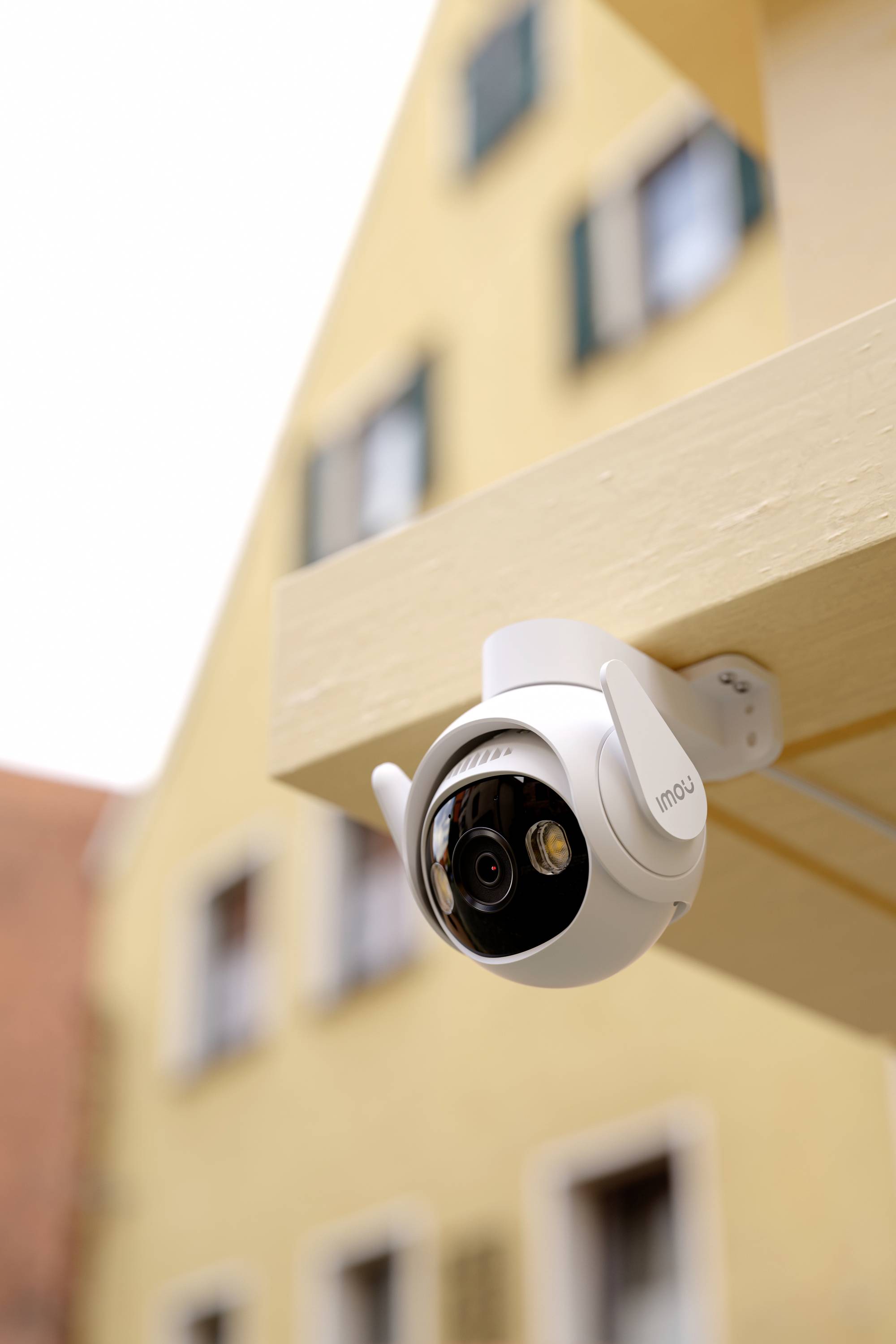 Caméra extérieure sur un bâtiment, avec en arrière-plan une maison jaune à plusieurs étages comportant plusieurs fenêtres.