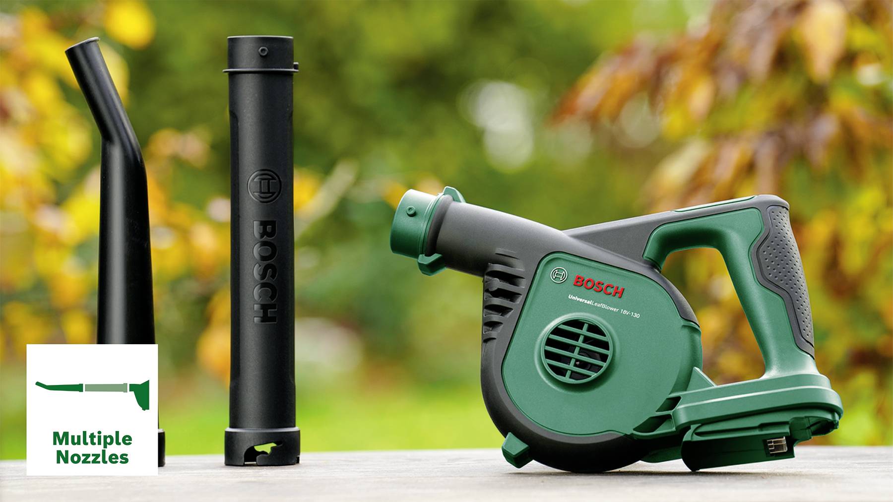 Un souffleur de feuilles portable vert de Bosch avec plusieurs buses, posé sur une table à l'extérieur ; des feuilles colorées en arrière-plan.