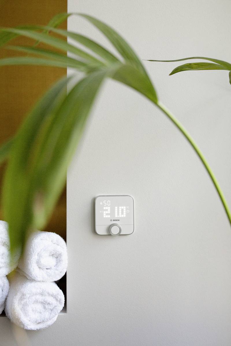 Un thermostat numérique affiche la température. Au premier plan, une feuille de plante d'intérieur, à côté de serviettes roulées.