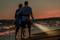 Un couple âgé se promène le long de la plage au coucher du soleil. L'homme tient une petite lanterne lumineuse à la main.