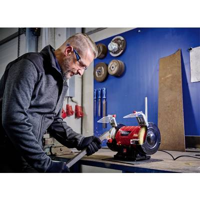 Un homme travaille une pièce métallique avec une meuleuse dans un atelier. Des étincelles volent, et des lunettes de protection et des gants sont visibles.