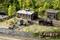 Un paysage ferroviaire miniature avec un petit dépôt de locomotives, des rails, une locomotive à vapeur noire et une forêt verte en arrière-plan.
