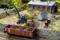 Scène de train miniature : Une petite pelleteuse charge du charbon dans un wagon de chemin de fer, à côté d'un bâtiment en briques rouges et d'un hangar bleu.