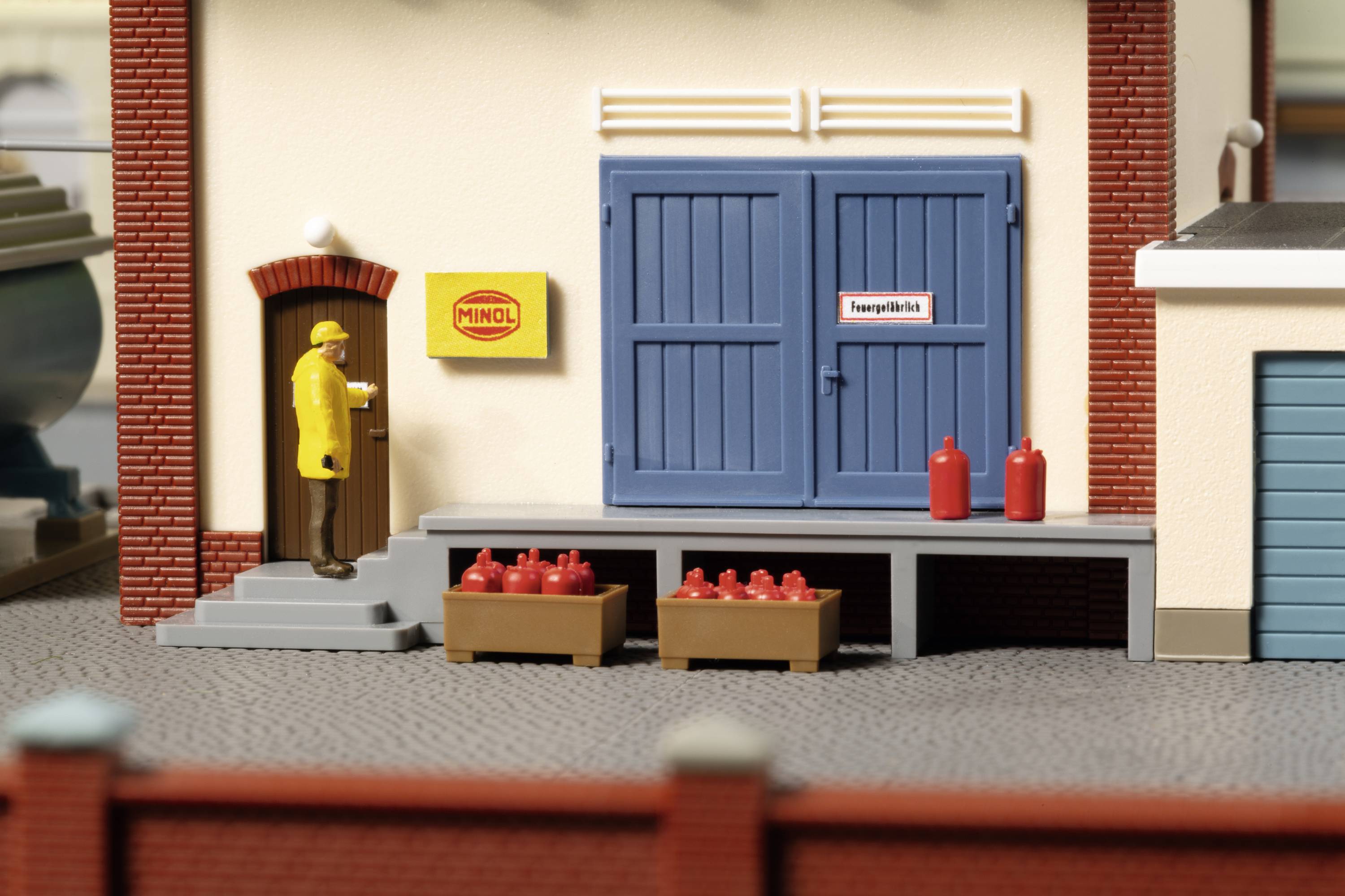 Une scène miniature montre un homme en imperméable jaune frappant à la porte d'un bâtiment aux portes bleues et aux briques rouges.