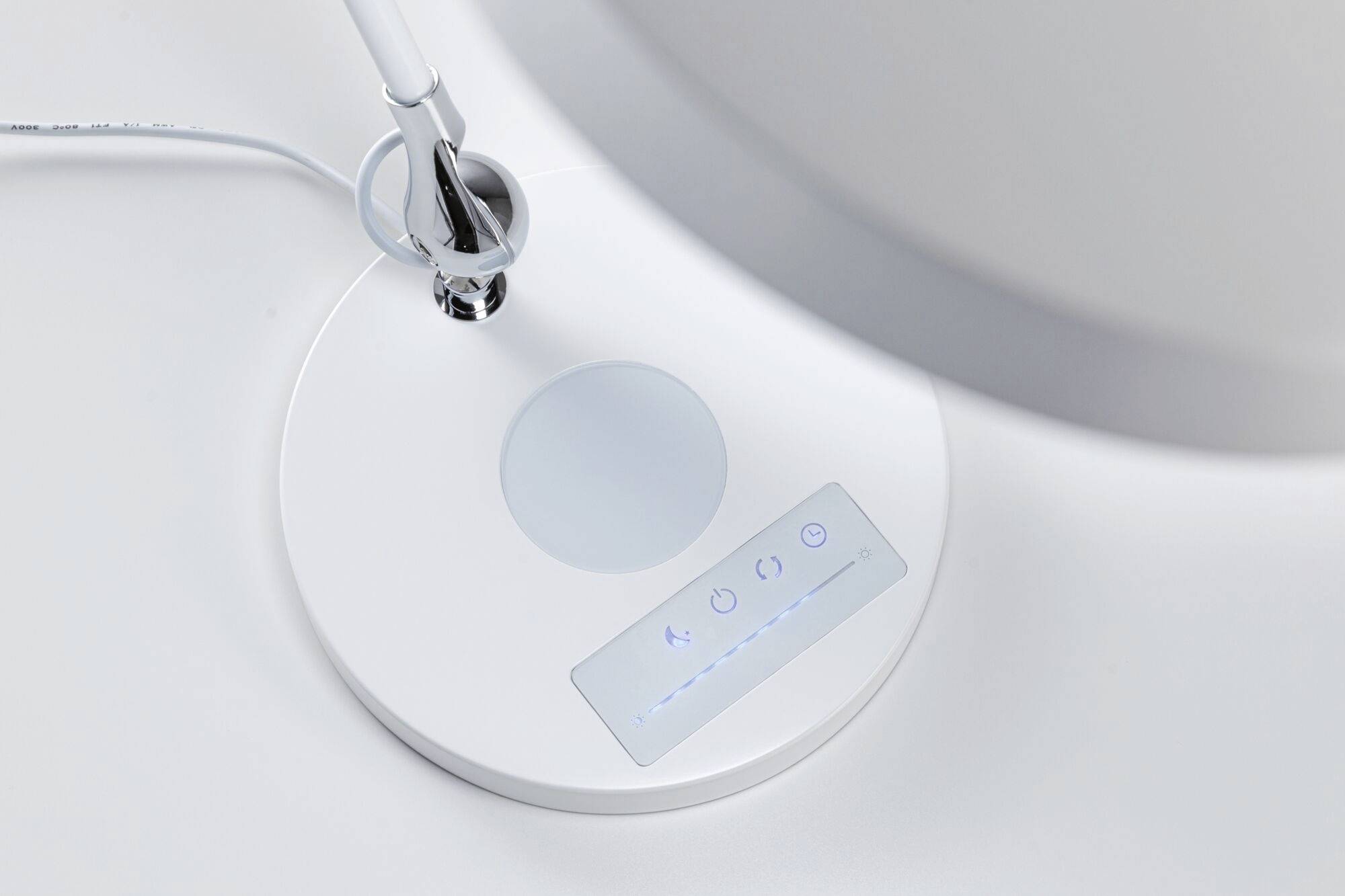 Un socle de lampe blanc avec un panneau de commande tactile et un élément lumineux circulaire. Un câble et une partie de l'abat-jour sont visibles.