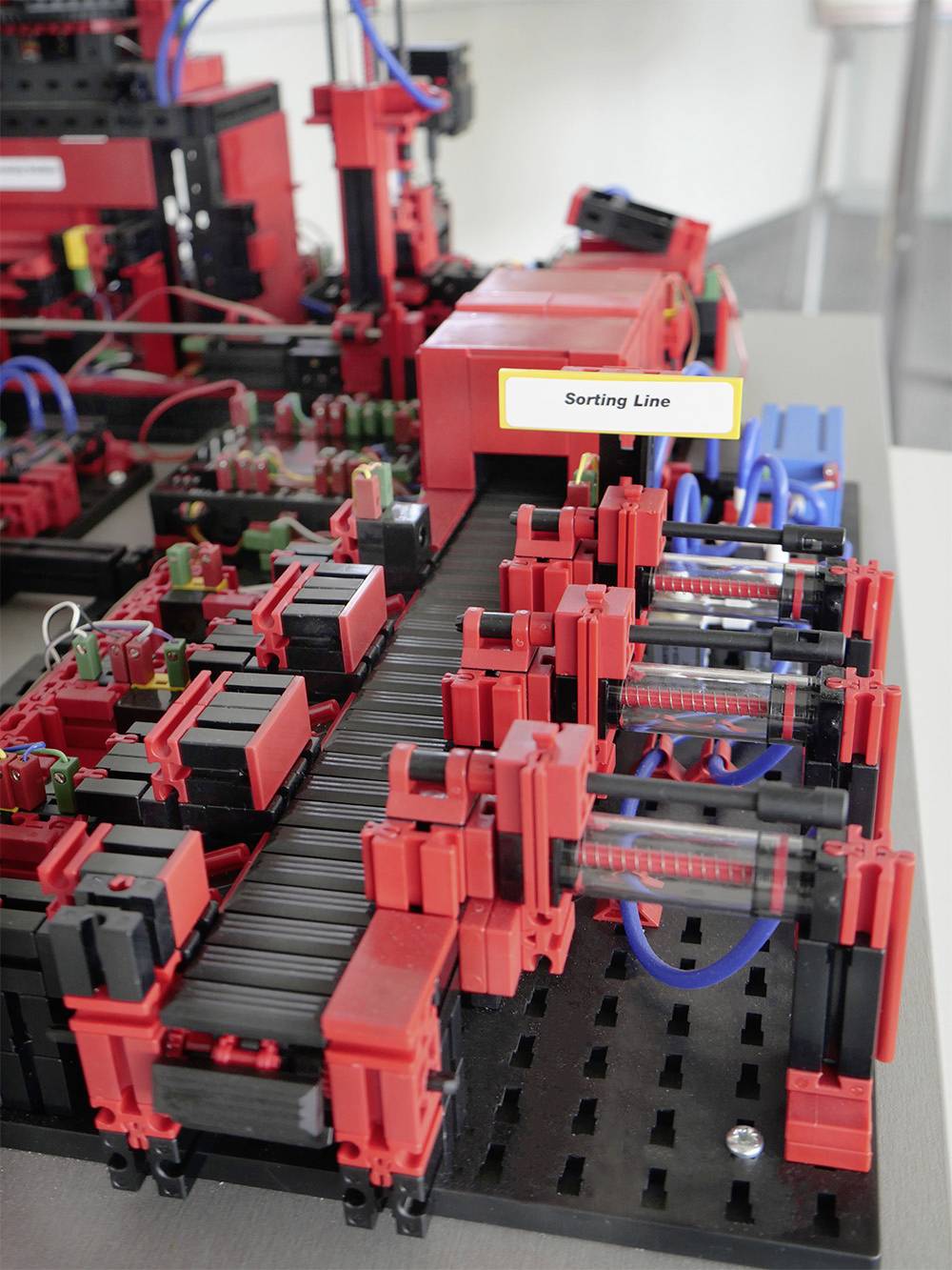 Une machine jouet rouge simule une ligne de tri. Des petits objets sont transportés sur un tapis roulant.