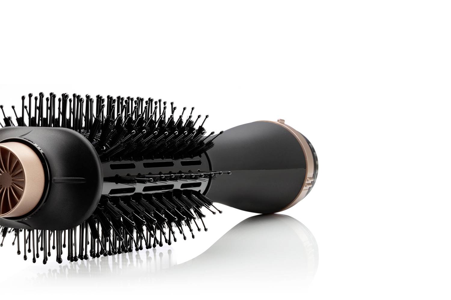 Un fer à friser noir et rond avec des poils pour brosser et styliser simultanément les cheveux. Il est posé sur une surface réfléchissante.
