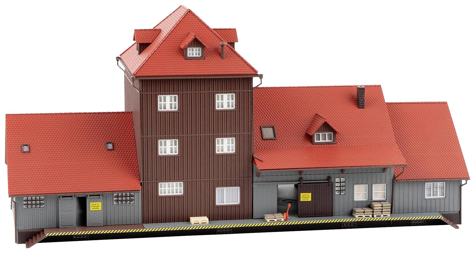 Modèle d'une gare de fret avec des toits rouges et des murs gris. Des cartons et des caisses sont placés sur le quai de chargement.