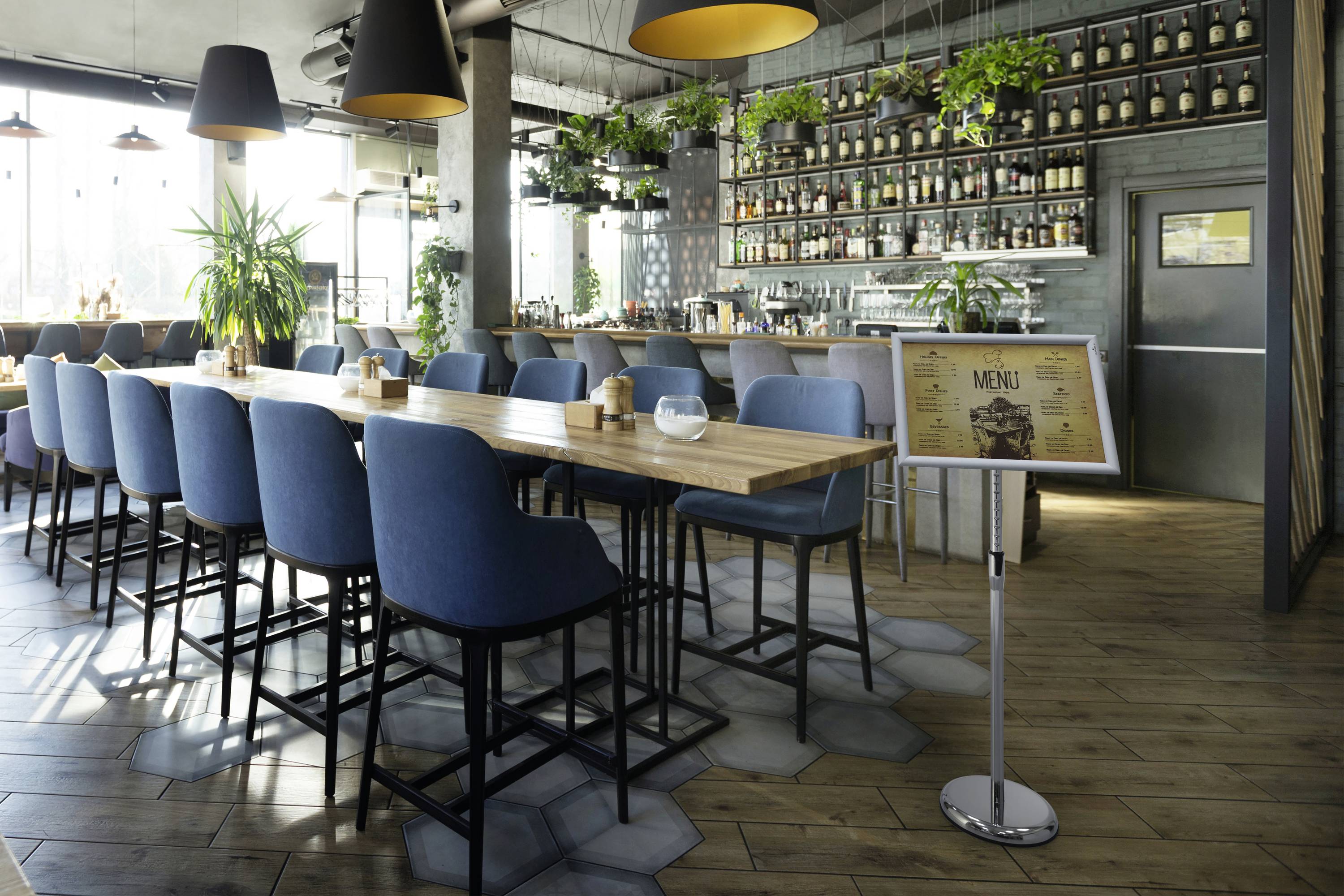 Un café moderne avec un long comptoir en bois, des chaises bleues et des plantes. Un tableau de menu est situé à droite du comptoir.