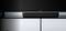Un téléviseur à écran plat est posé sur un buffet noir moderne. En dessous se trouve une barre de son étroite et noire.