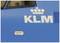 Train bleu avec le logo KLM, avec des représentations esquissées du réseau ferroviaire néerlandais, incluant 'Amsterdam CS' et 'Schiphol'.