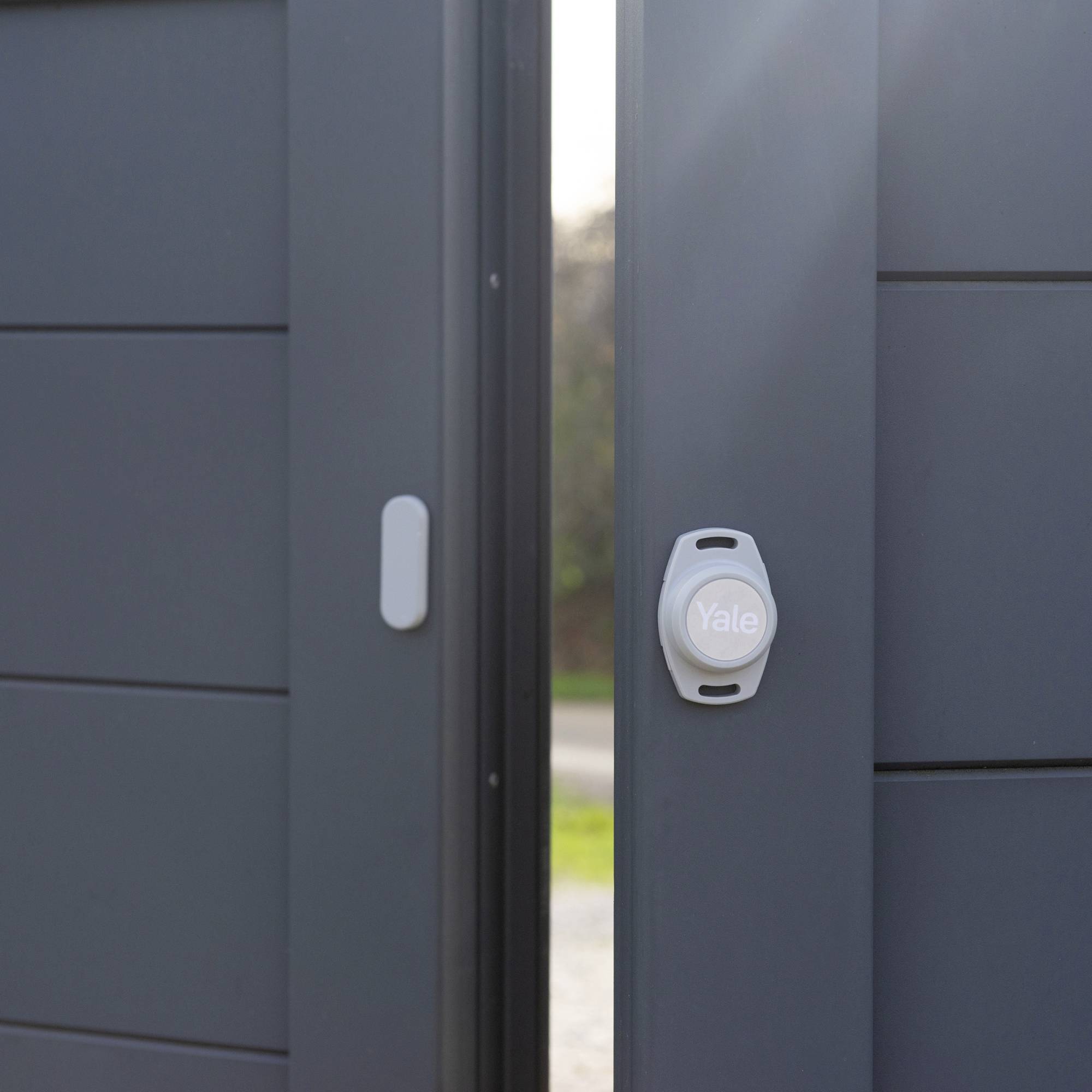 Serrure de sécurité grise sur une porte d'entrée moderne, légèrement entrouverte, avec de la lumière naturelle en arrière-plan.