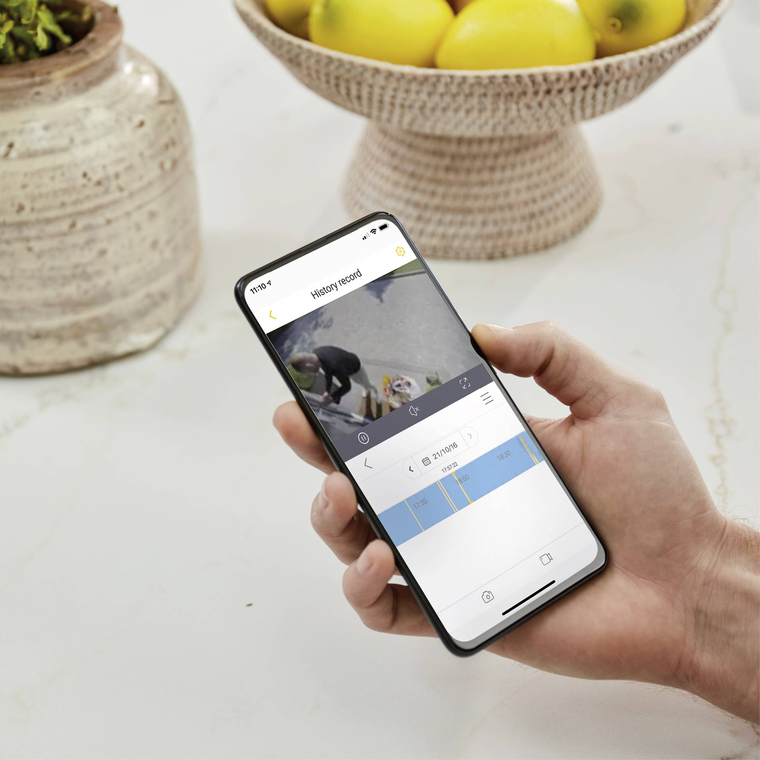 Une personne tient un smartphone avec l'interface d'une application de planification ouverte, au-dessus duquel se trouve un bol de citrons sur une table claire. L'accent est mis sur la planification numérique.