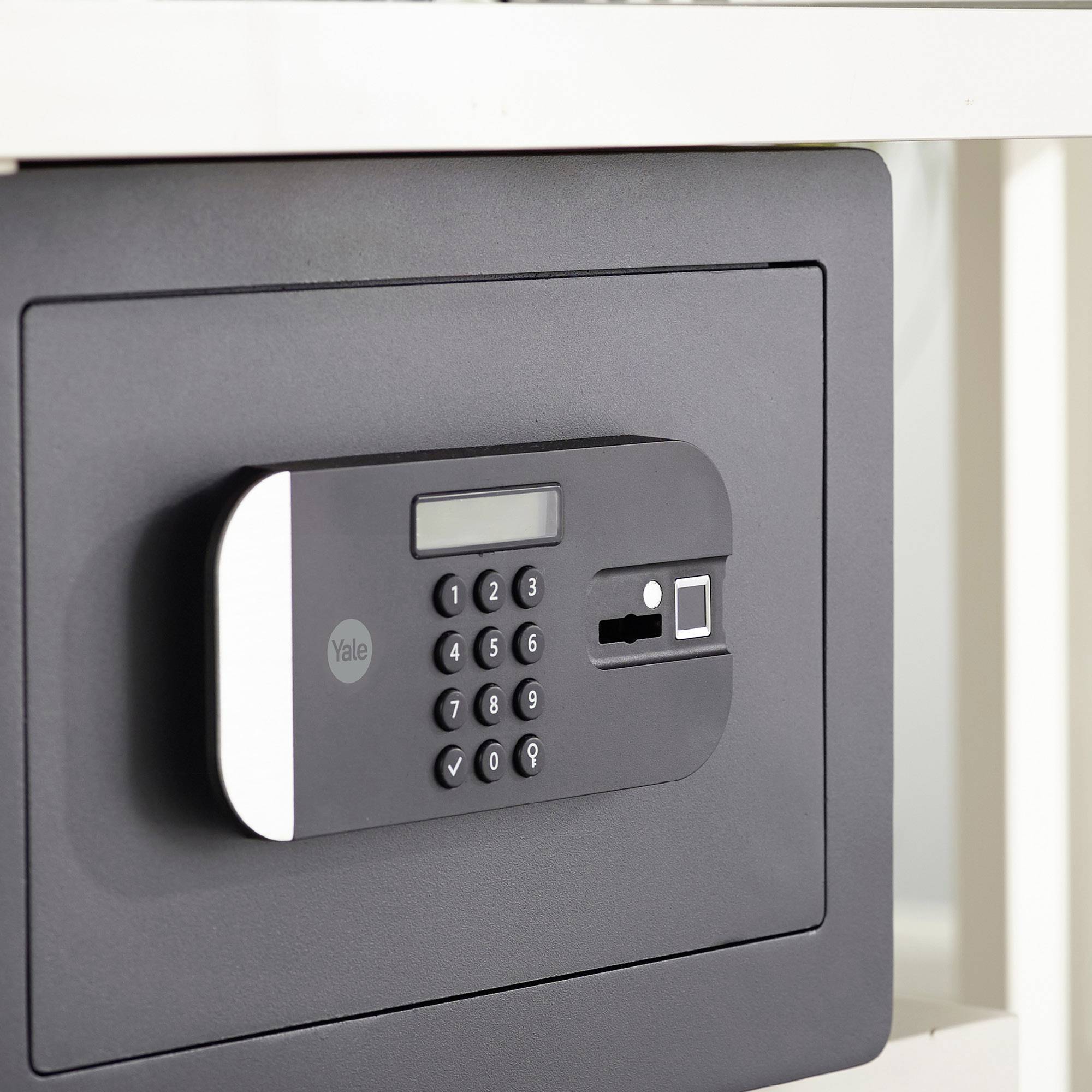 Un coffre-fort gris avec un clavier à code numérique et un lecteur d'empreintes digitales sur la façade, intégré dans un meuble.