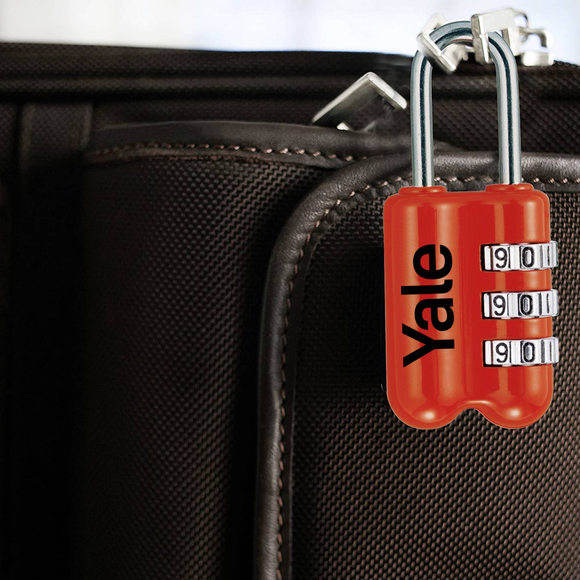 Un cadenas rouge à chiffres sécurise la fermeture éclair d'une valise. La valise est noir-brun.