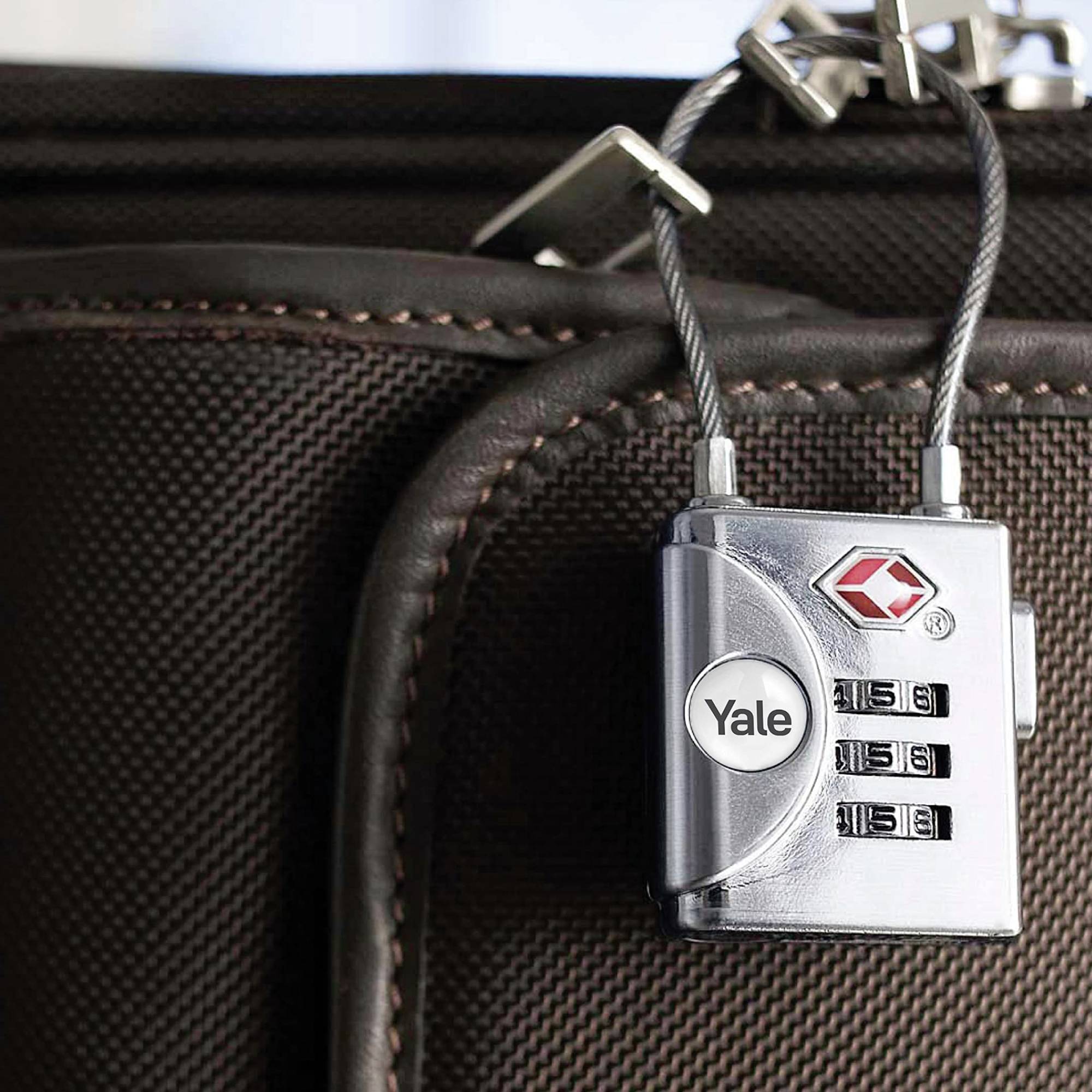 Un cadenas argenté est fixé sur une valise brune. Le cadenas affiche les chiffres '315', symbolisant la sécurité du voyage.