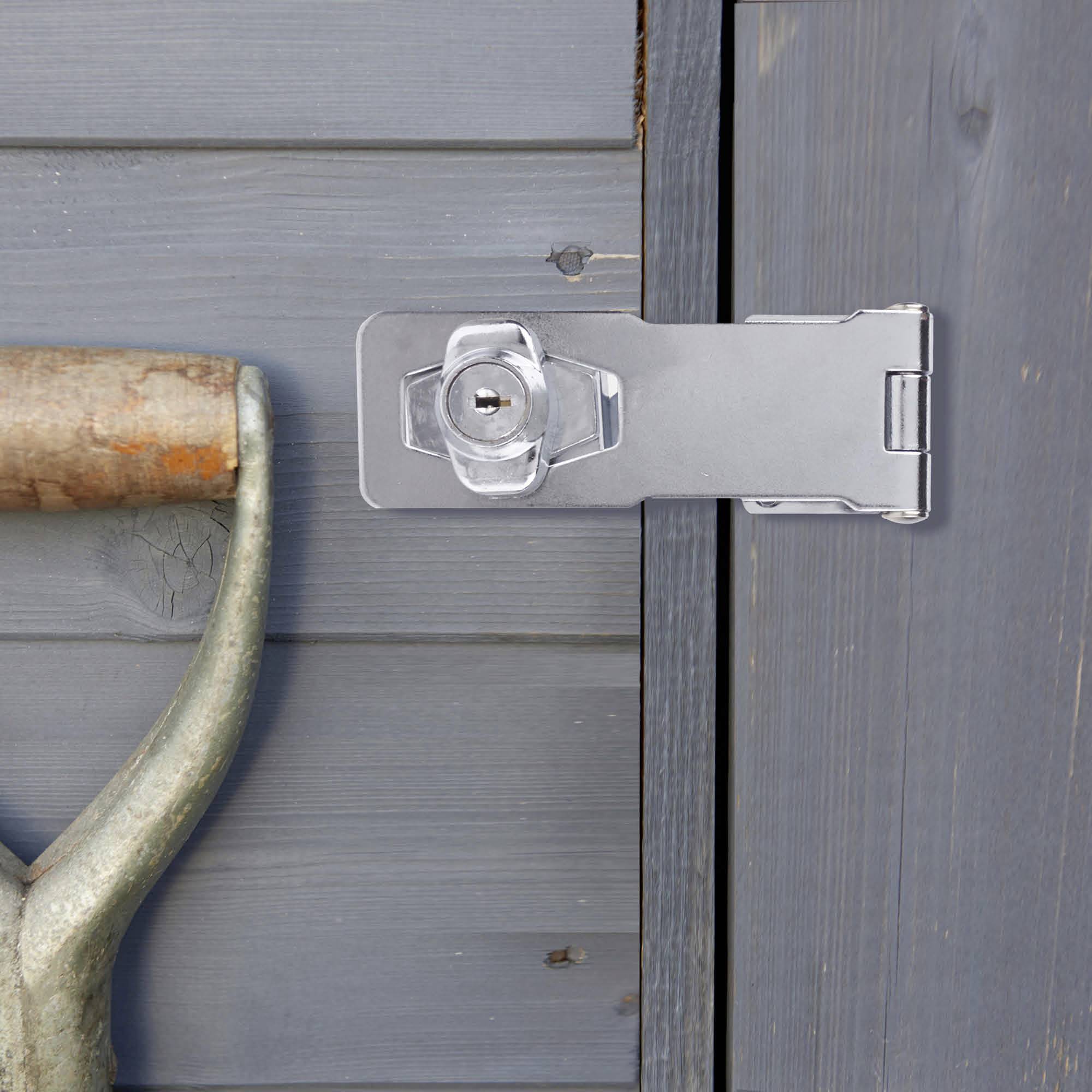 Une porte en bois fermée avec un cadenas argenté. À gauche, une pelle au manche en bois appuyée contre la porte.