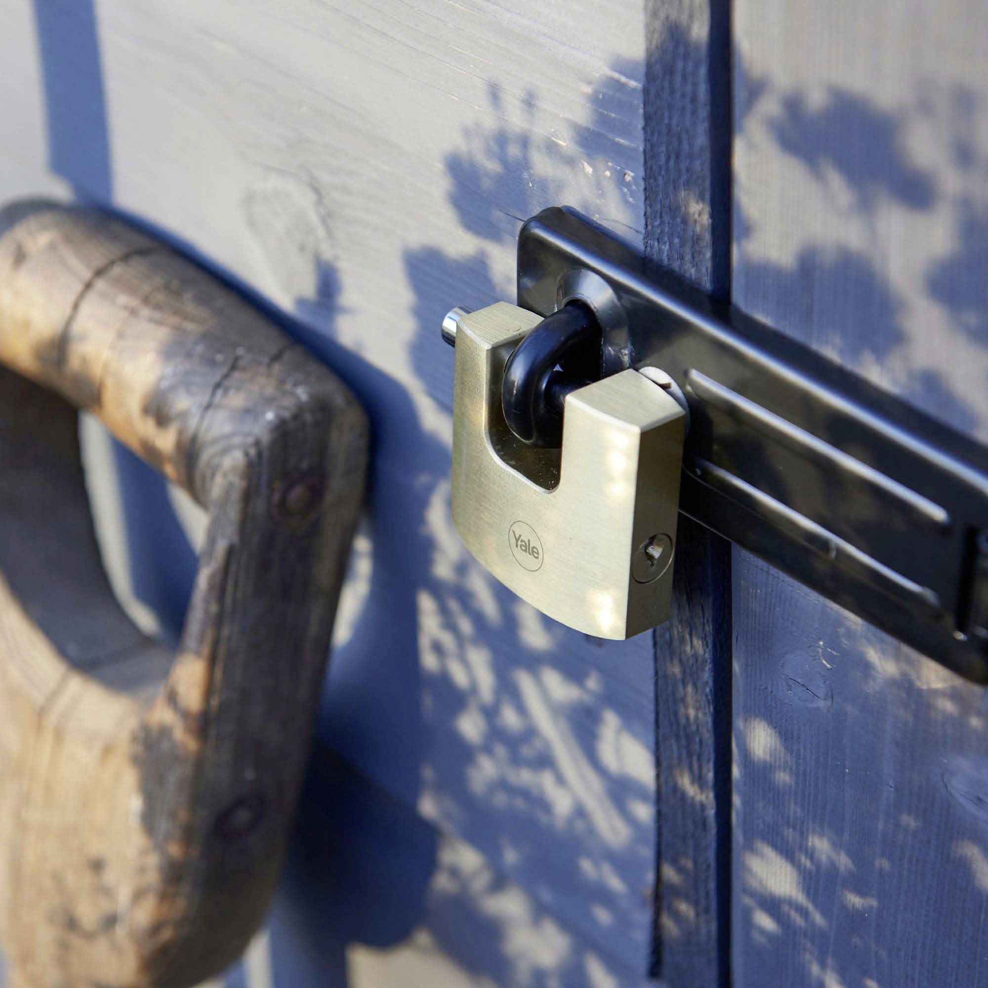 Un cadenas massif sécurise une porte de grange en bois. La lumière du soleil projette des motifs d'ombre sur la porte bleue.