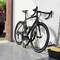 Un vélo de course noir est appuyé contre un mur de garage blanc et sécurisé par un cadenas. À droite se trouvent des outils et un carton.