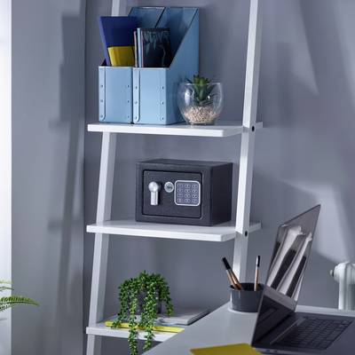 Une étagère blanche avec un petit coffre-fort, des classeurs de bureau et des plantes posés dessus dans un bureau moderne. Une table avec des stylos est placée devant.