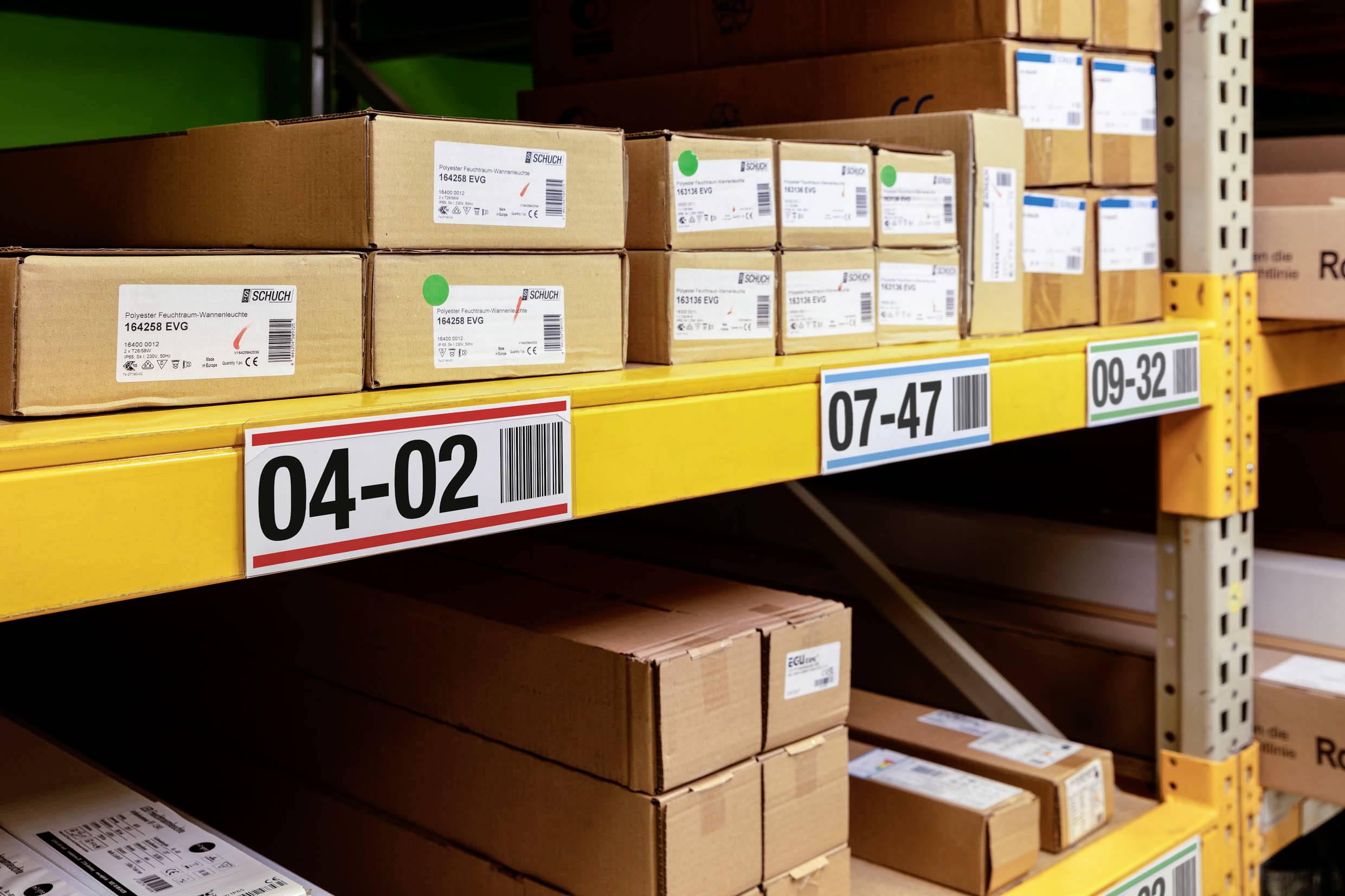 Étagère avec compartiments numérotés, remplie de cartons empilés. Les étiquettes affichent les informations sur les produits et les numéros de série.