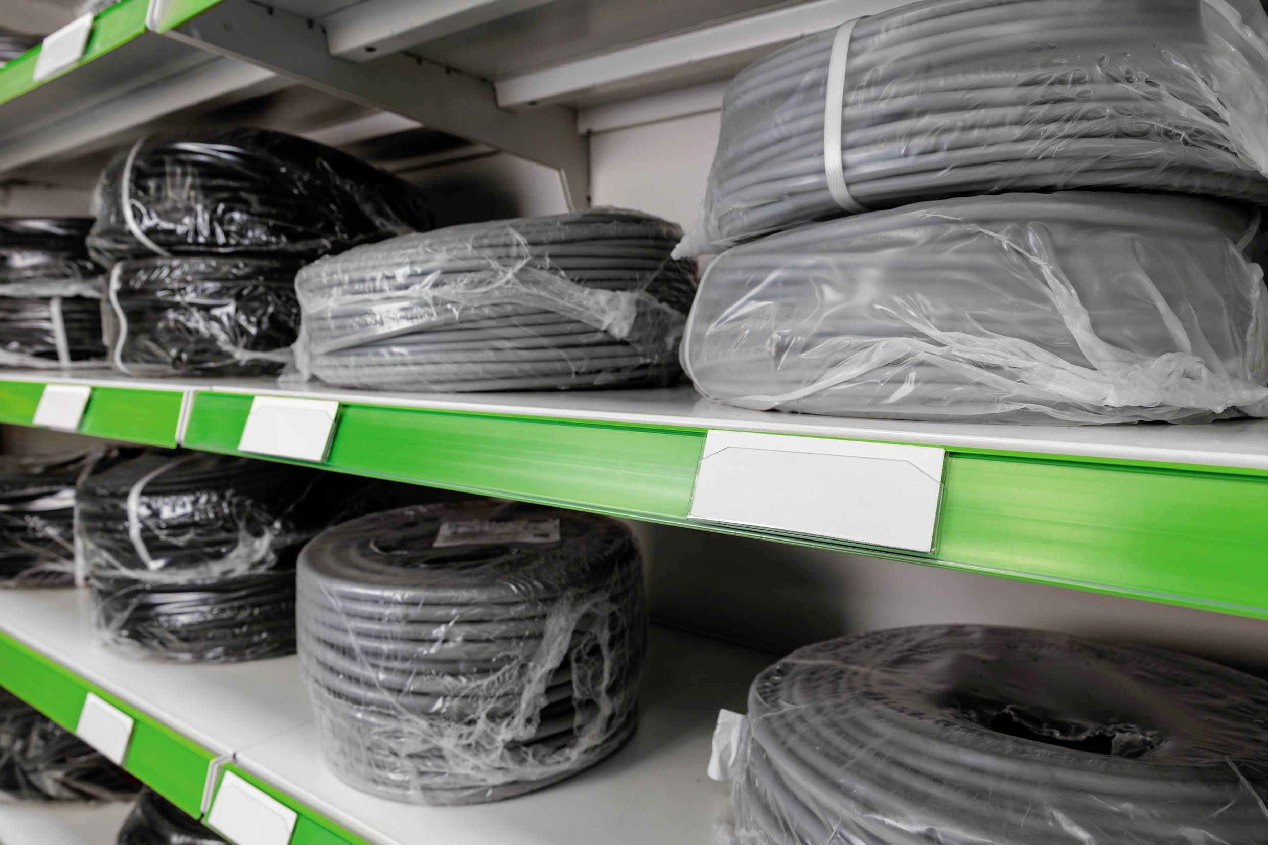 Plusieurs bobines de câbles dans des emballages en plastique sont posées sur des étagères vertes dans un magasin.