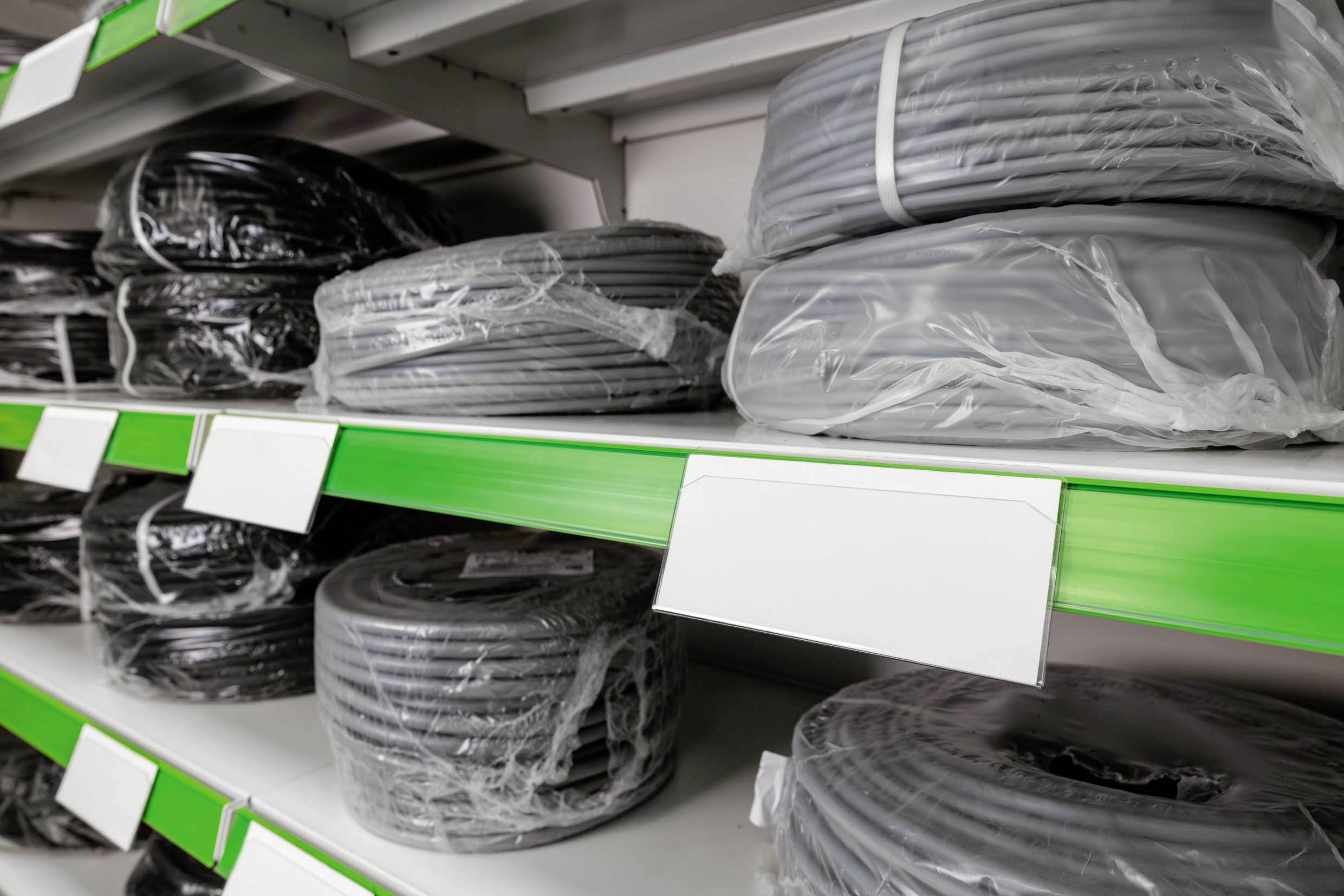 Des bobines de câbles sont rangées sur une étagère. Les bobines sont emballées dans du plastique et empilées à différents niveaux.