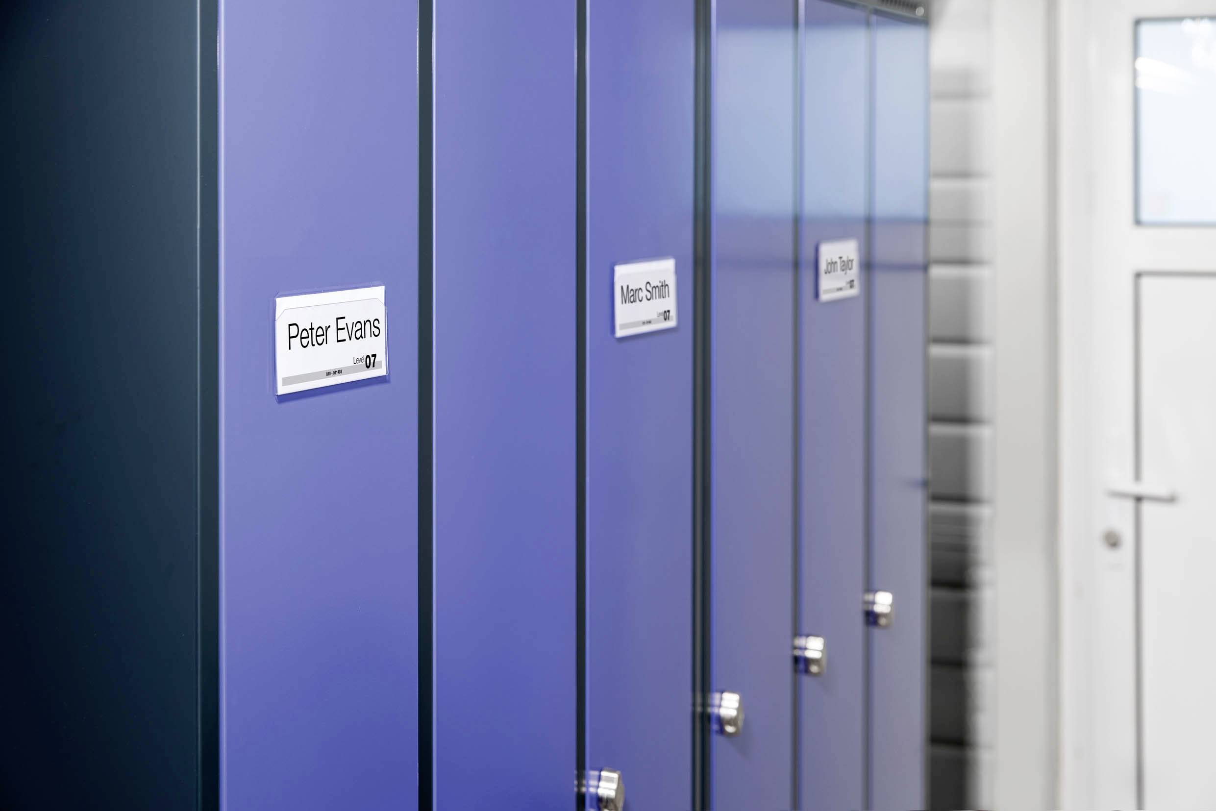 Casiers bleus avec des étiquettes nominatives dans un couloir. Une porte est visible à droite en arrière-plan.