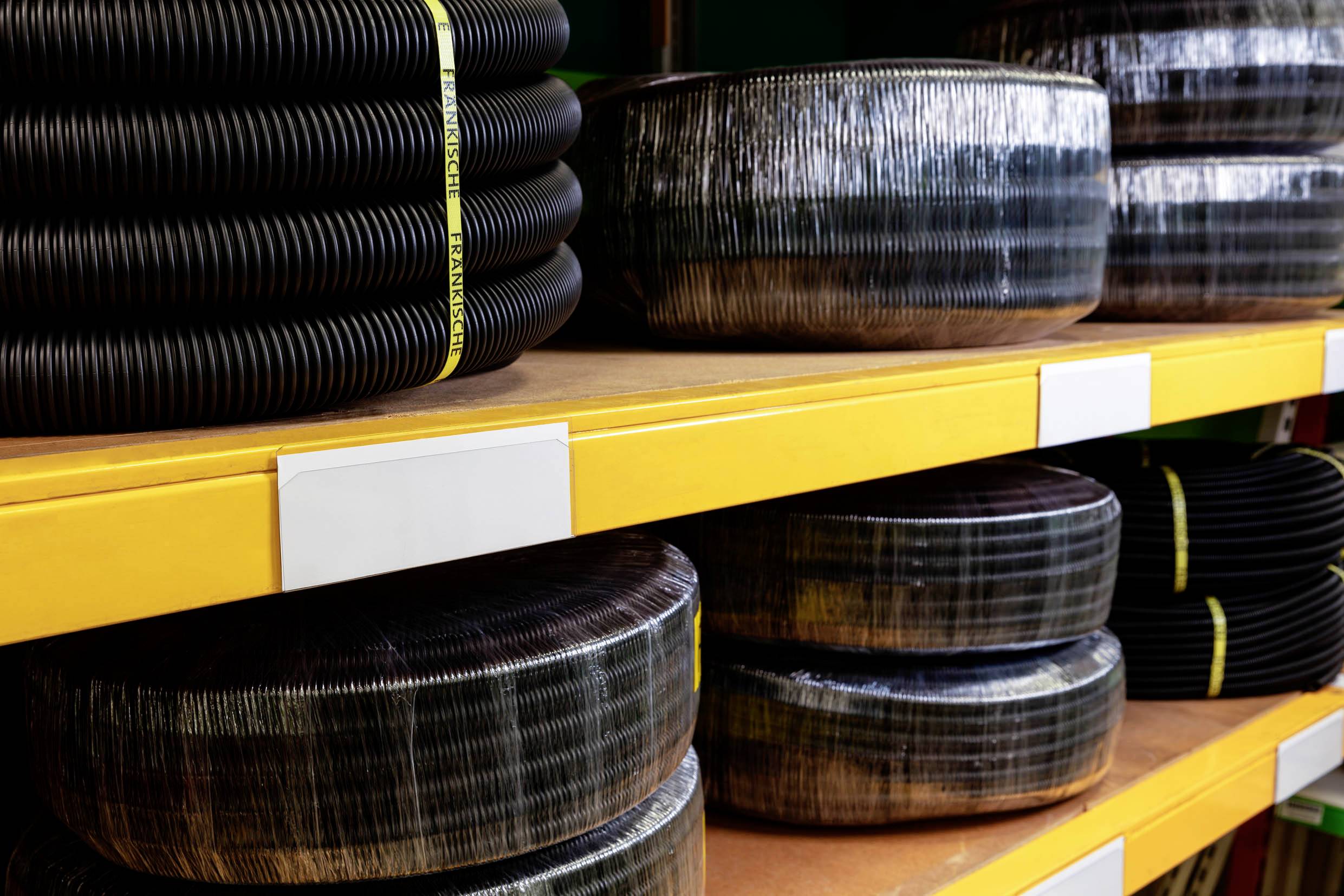 Étagères avec des rouleaux de tubes en plastique noir stockés, enveloppés de film. Les étagères sont jaunes.