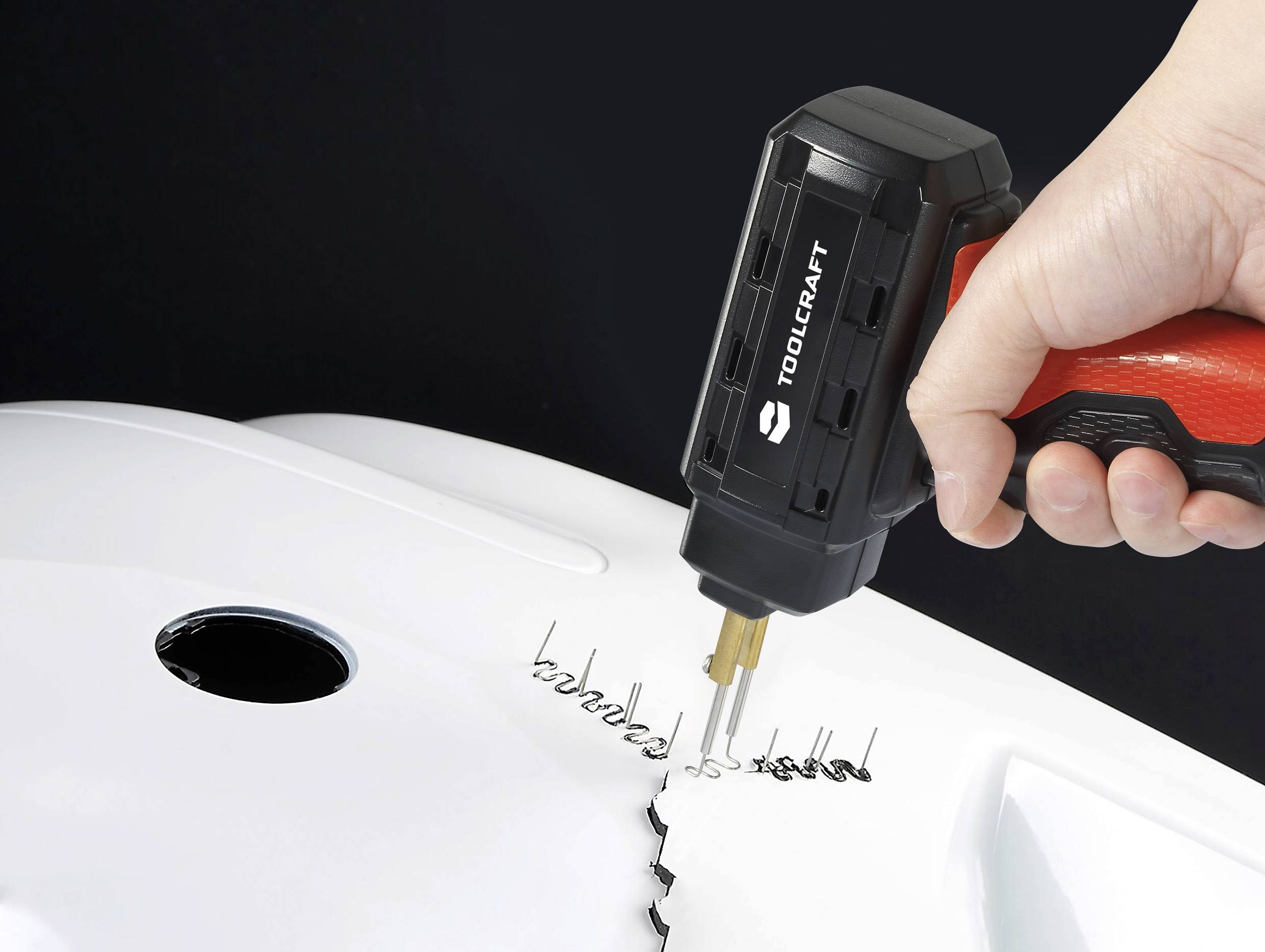 Une main tient un fer à souder électrique lors du soudage d'une surface blanche en plastique.