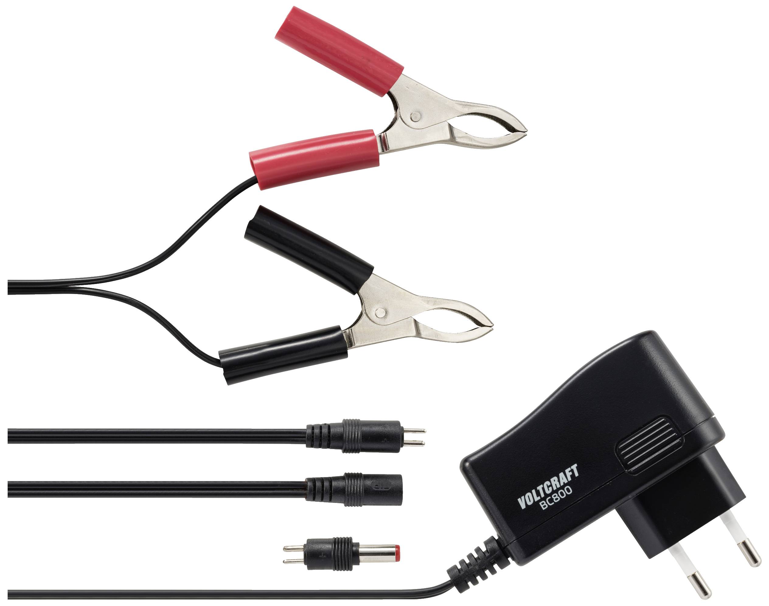 Chargeur de batterie avec des pinces rouges et noires, différents câbles adaptateurs et bloc d'alimentation. Nom de marque 'Voltcraft BC-600' sur le bloc d'alimentation.