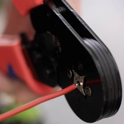 'Une personne utilise un outil de sertissage pour connecter un fil rouge.'