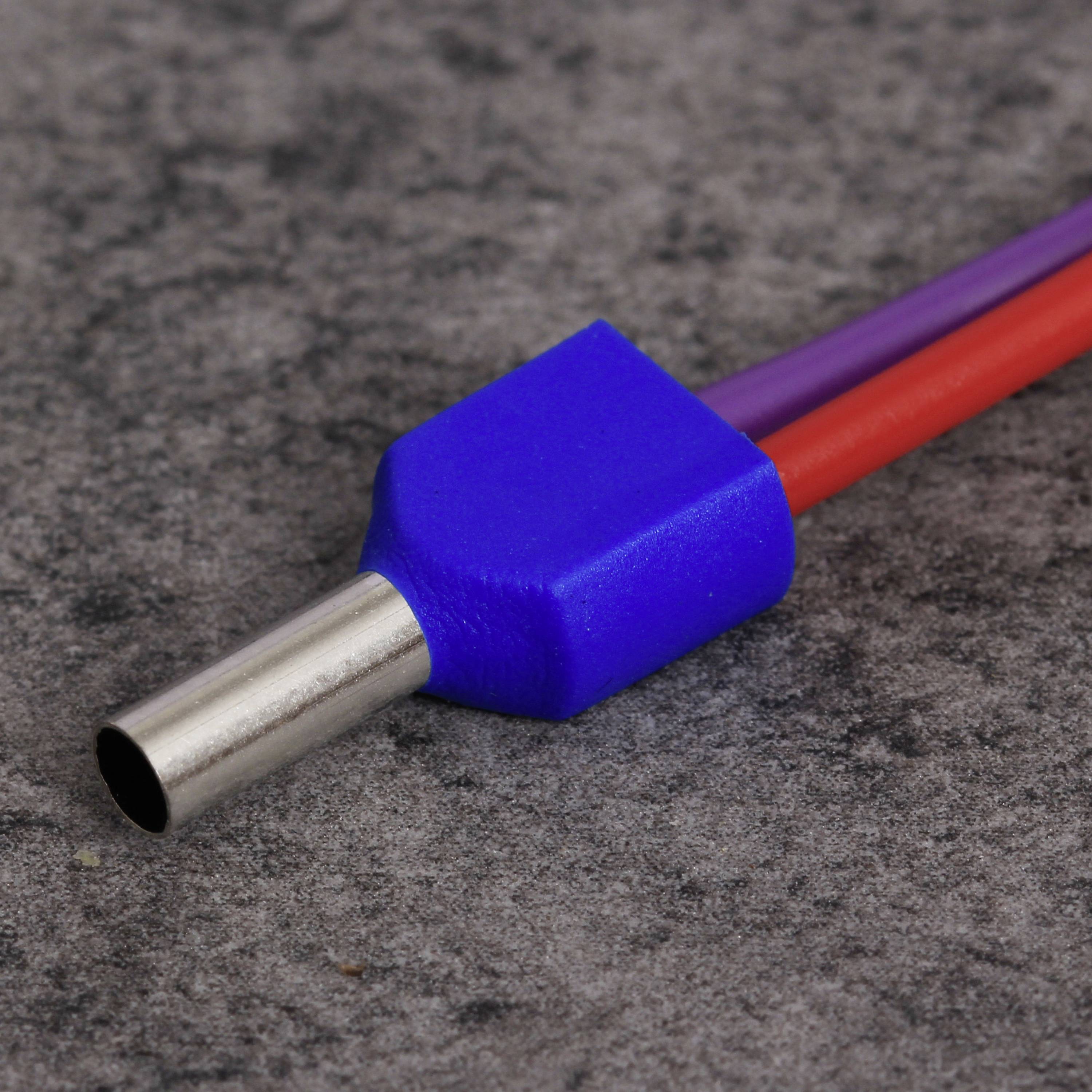 Une fiche métallique bleue avec deux câbles, l'un rouge et l'autre violet, est posée sur une surface grise.