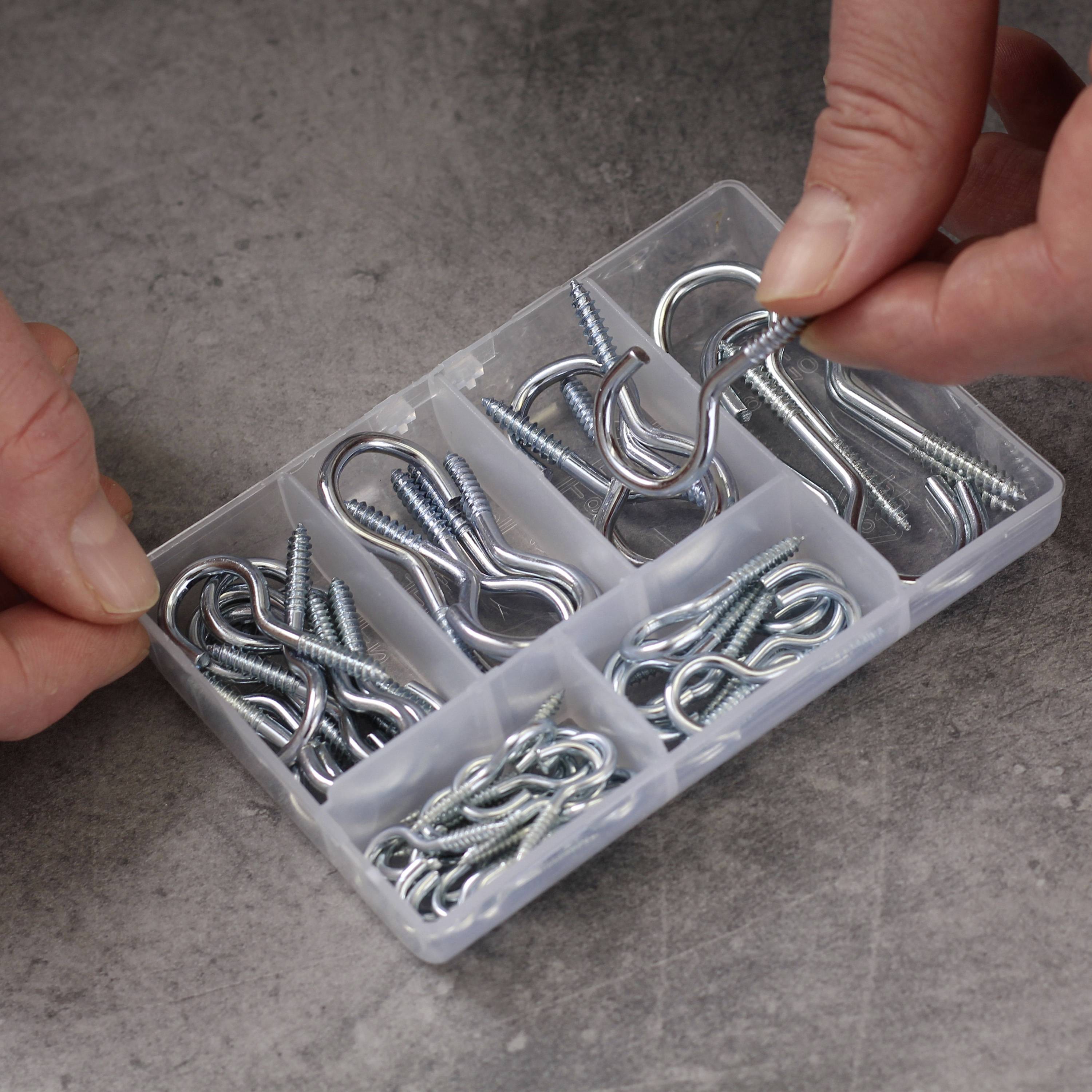 Une boîte en plastique contient divers crochets et vis métalliques. Deux mains saisissent un crochet en S.
