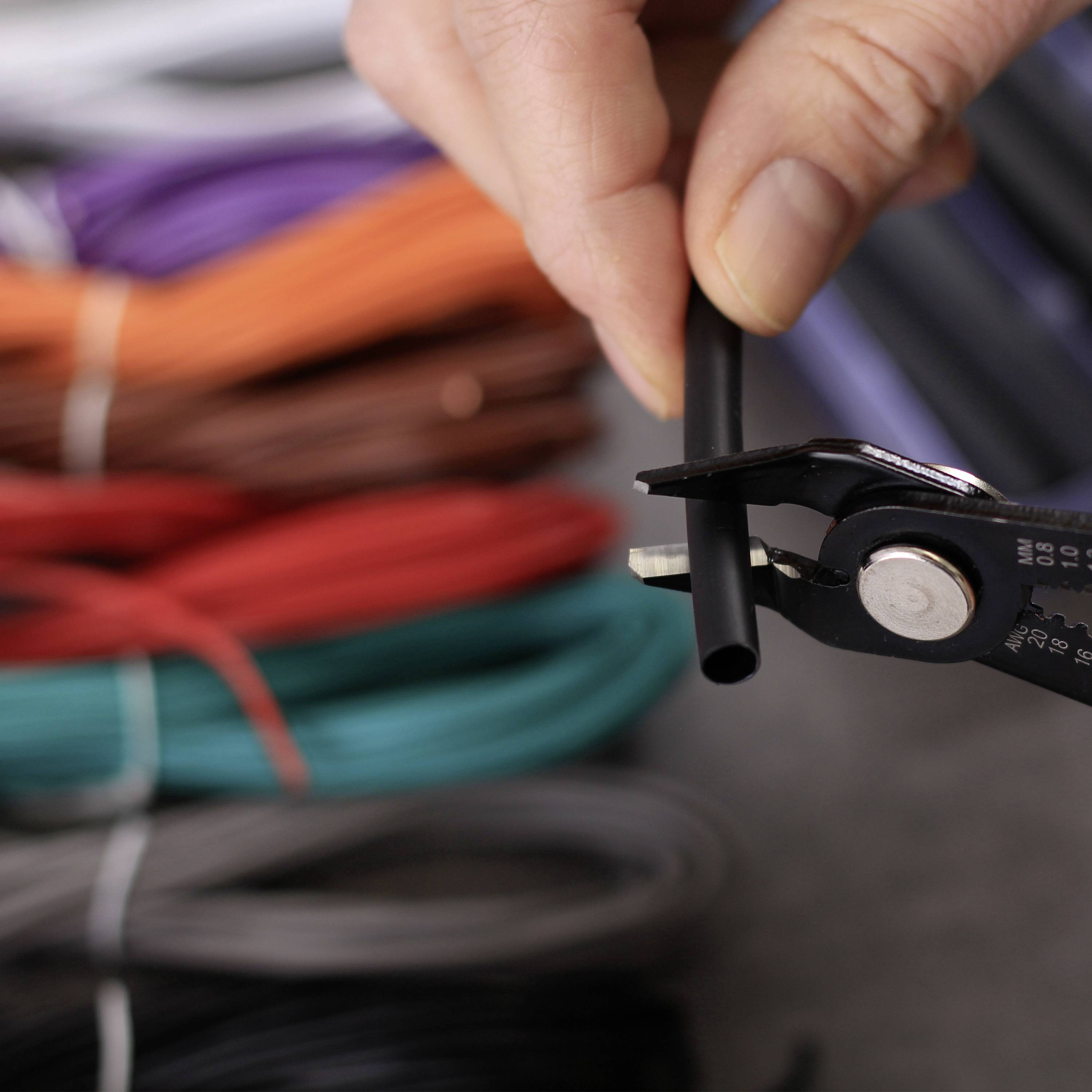 Une main tient un coupe-câble et coupe un câble noir. À l'arrière-plan, on peut voir différents rouleaux de câbles colorés.