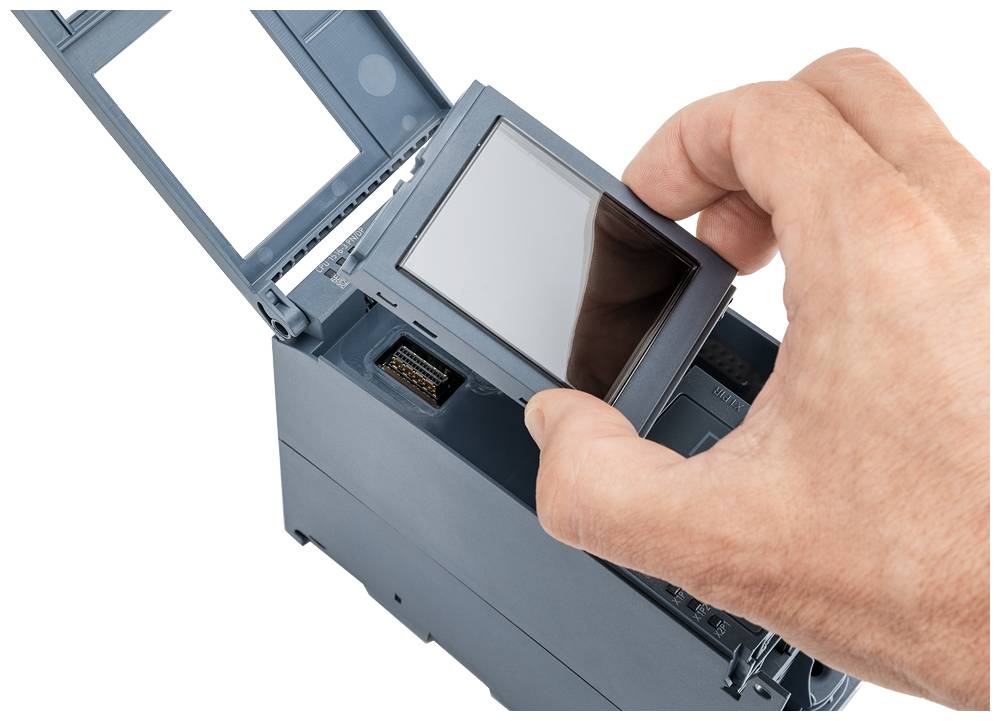 Une main installe un petit écran rectangulaire sur un appareil électronique dont le boîtier est ouvert.