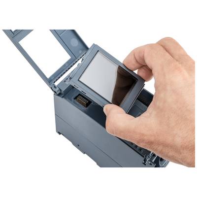 Une main installe un petit écran rectangulaire sur un appareil électronique dont le boîtier est ouvert.