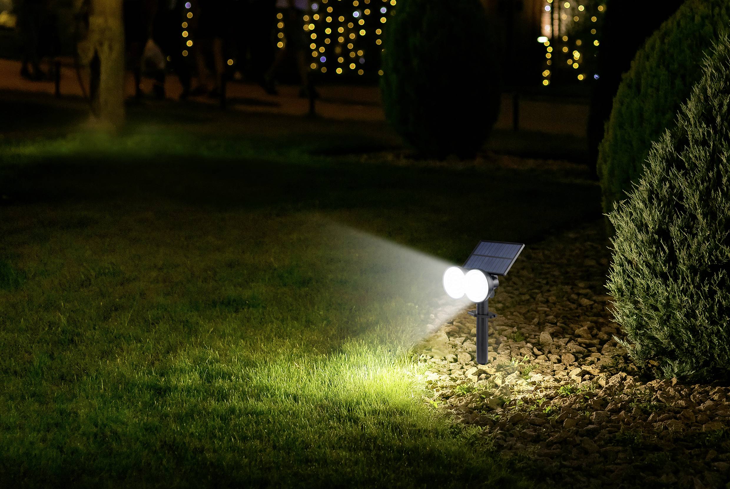 Une lampe solaire éclaire un chemin de jardin la nuit. Des arbres et des lumières floues sont visibles en arrière-plan.