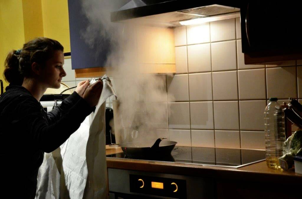 Une personne tient un chiffon pour dissiper la vapeur qui s'élève d'une poêle chaude sur une cuisinière dans un environnement de cuisine.
