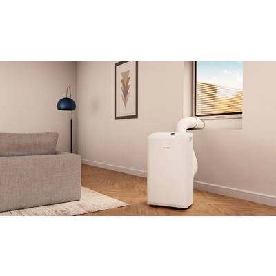 Un climatiseur portable est branché à une fenêtre dans un salon moderne. À côté se trouve un abat-jour bleu et blanc.