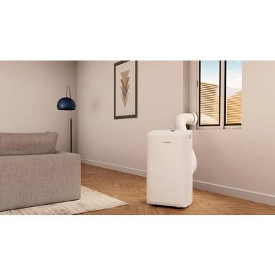 Climatiseur portable dans un salon moderne, connecté à une fenêtre. Une lampadaire se trouve à côté d'un canapé gris.