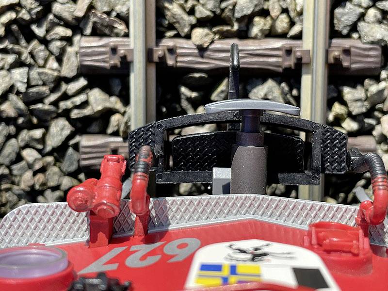 Gros plan d'un train miniature rouge portant le numéro '62' sur les rails, avec des pierres de ballast et des traverses ferroviaires visibles en arrière-plan.