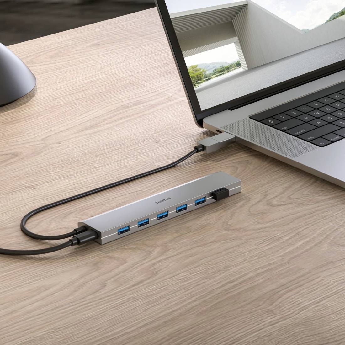 Un ordinateur portable posé sur une table avec un hub USB connecté, offrant plusieurs ports USB bleus, un bâtiment moderne en arrière-plan.