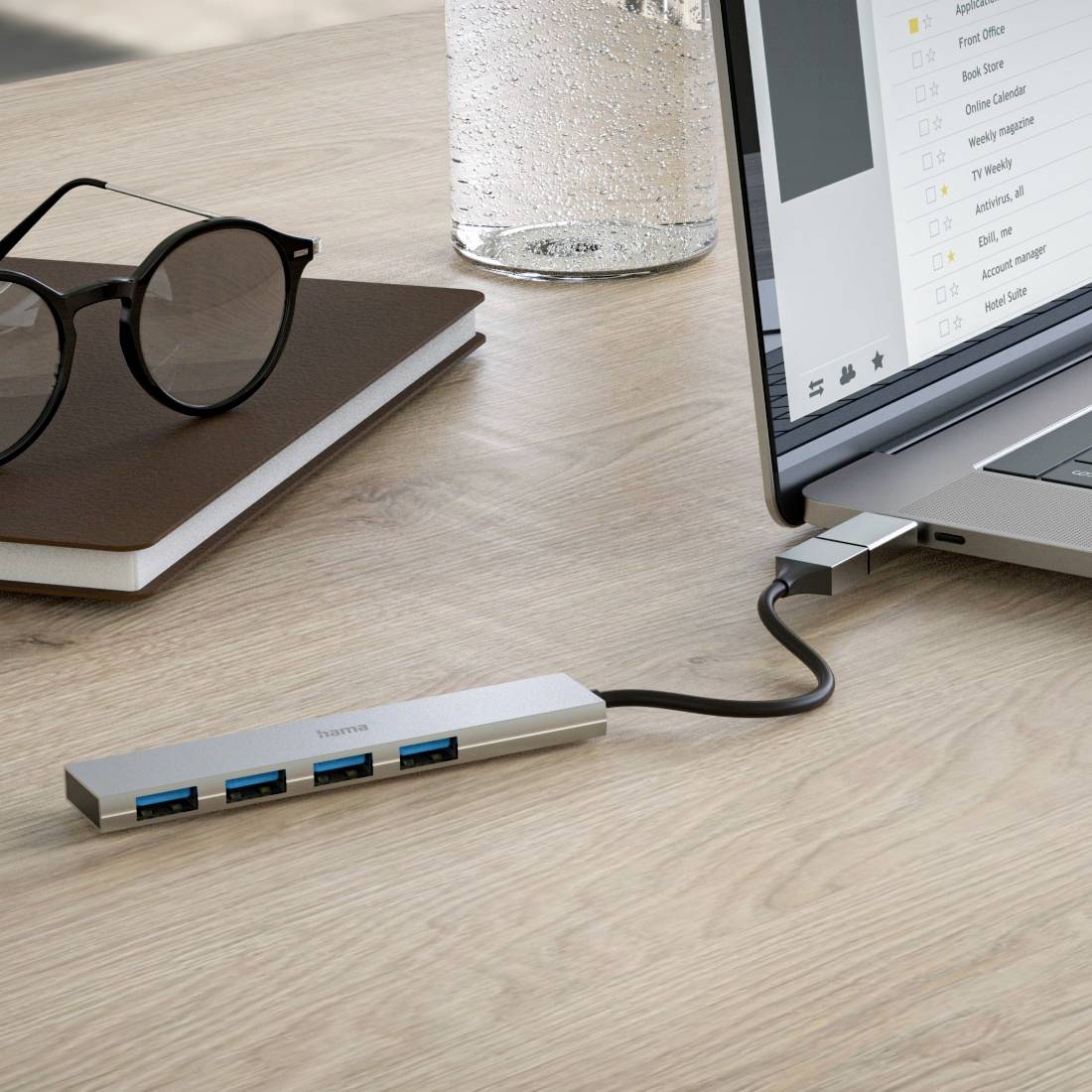 Un ordinateur portable est connecté à plusieurs périphériques USB via un hub USB-C. Sur la table sont posés des lunettes et un carnet de notes.